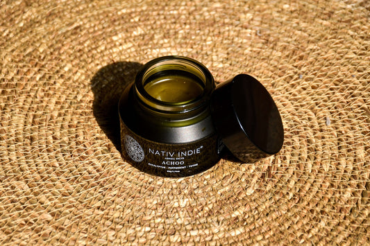 Jar of Achoo Herbal Salve on woven mat, showcasing organic skincare made with authentic ingredients from the Himalayas.